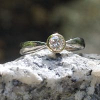 Brillant in konischer Gelbgold-Fassung in zur Fassung spitz zulaufender Weißgoldschiene